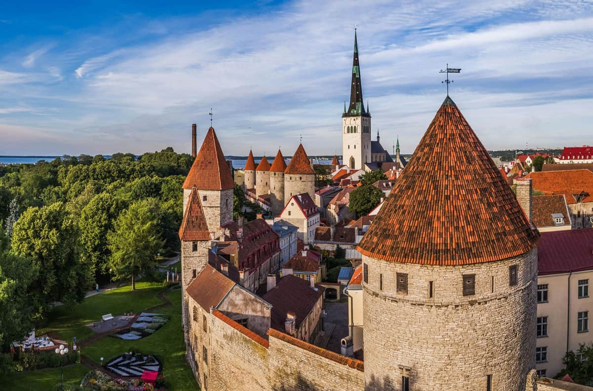 Tallinn Card – Vabamu Museum of Occupations and Freedom and 5 other attractions Aerial view of a historic town with stone walls, red-roofed towers, and a tall church spire surrounded by greenery.