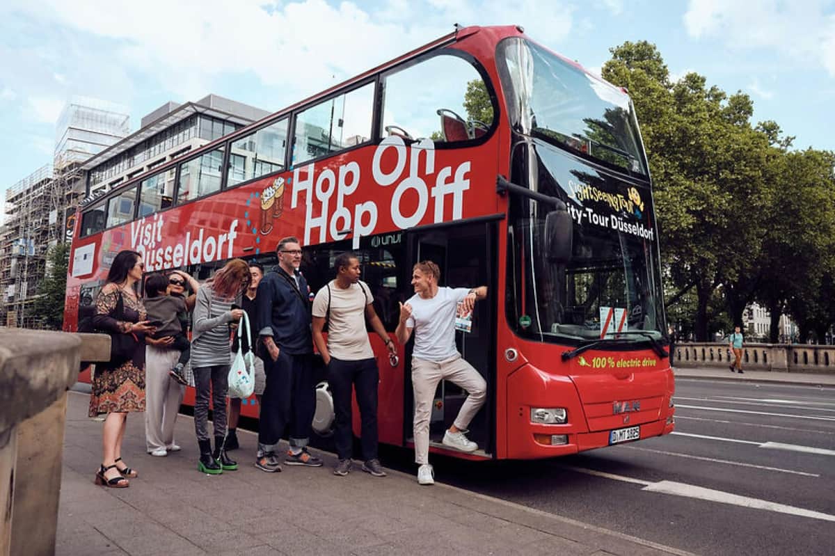 DüsseldorfCard Plus: 48, 72, or 96-Hr Public Transport (Düsseldorf) A group of people standing near a red double-decker sightseeing bus with "Hop On Hop Off" written on its side.