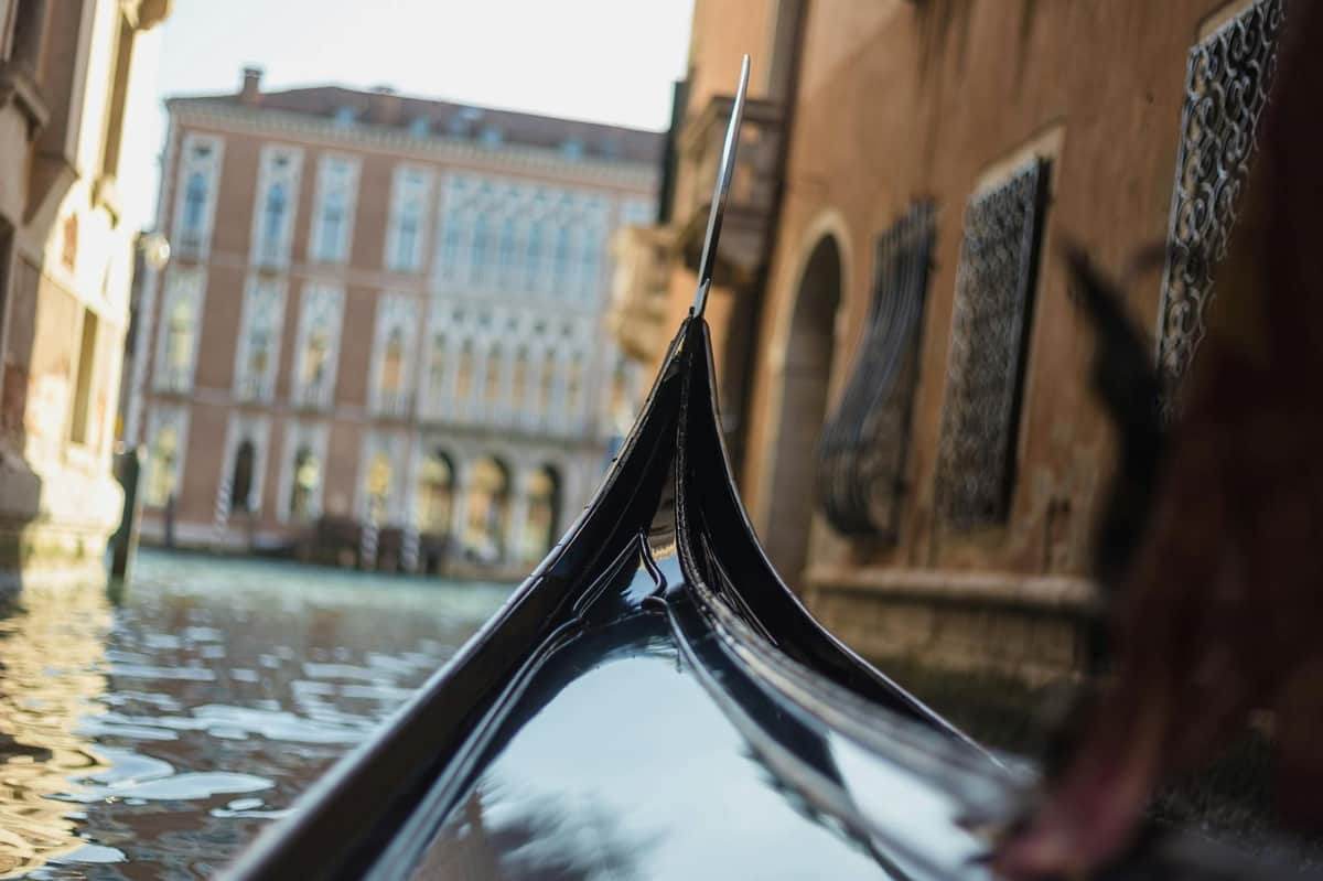 Plavba na gondole a Murano, plavba lodí Burano (Benátky) Detailní záběr přídě gondoly proti kanálu s historickými budovami a vodou v pozadí v italských Benátkách.