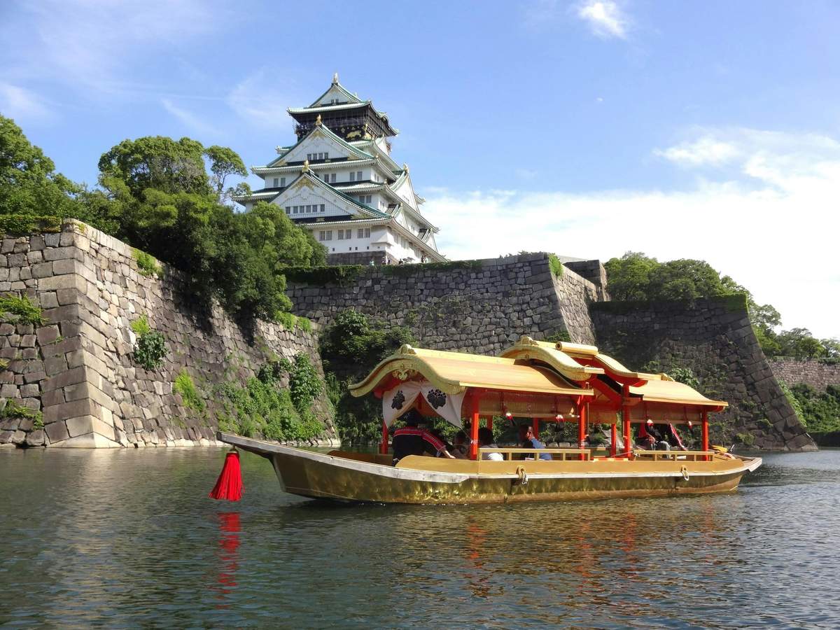 Osaka: e-Pass Premium (1 Day) (Suita) A traditional boat with a golden roof on a moat near a historic Japanese castle surrounded by stone walls and greenery.