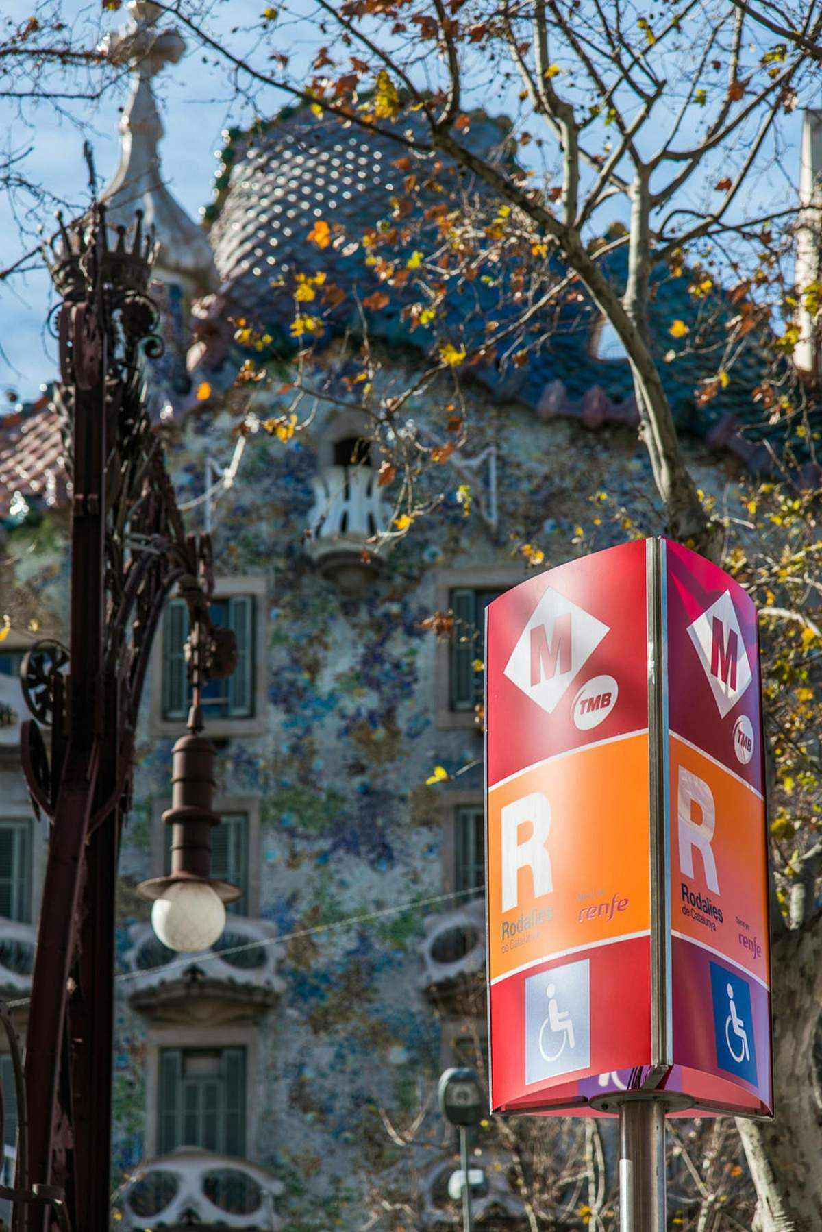 Před barevnou, okrasnou budovou se stromy a dekorativní pouliční lampou je nápis označující stanice metra a RENFE.