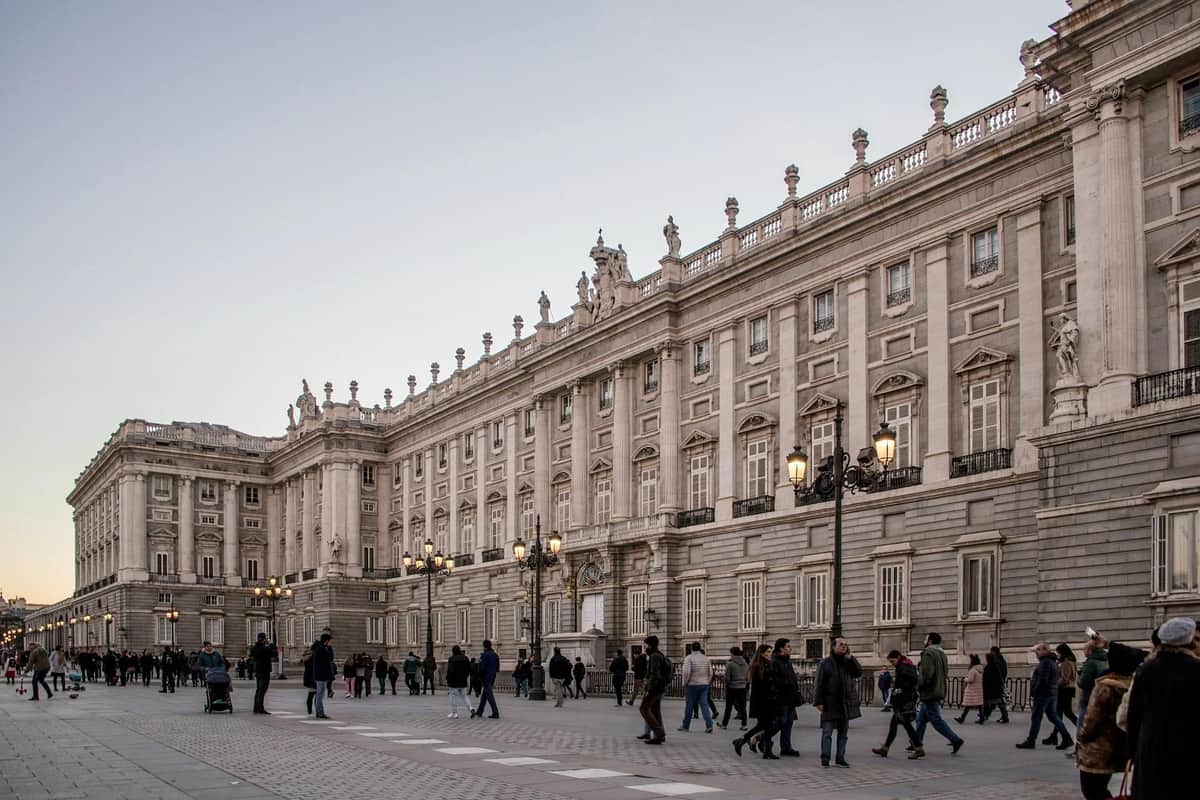 Large stone building with ornate details and columns, surrounded by numerous pedestrians on a spacious paved plaza.