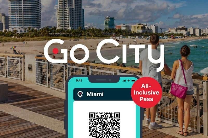 Un smartphone affiche un code QR "Miami All-Inclusive Pass". En arrière-plan, des personnes marchent sur la promenade d'une plage de Miami.