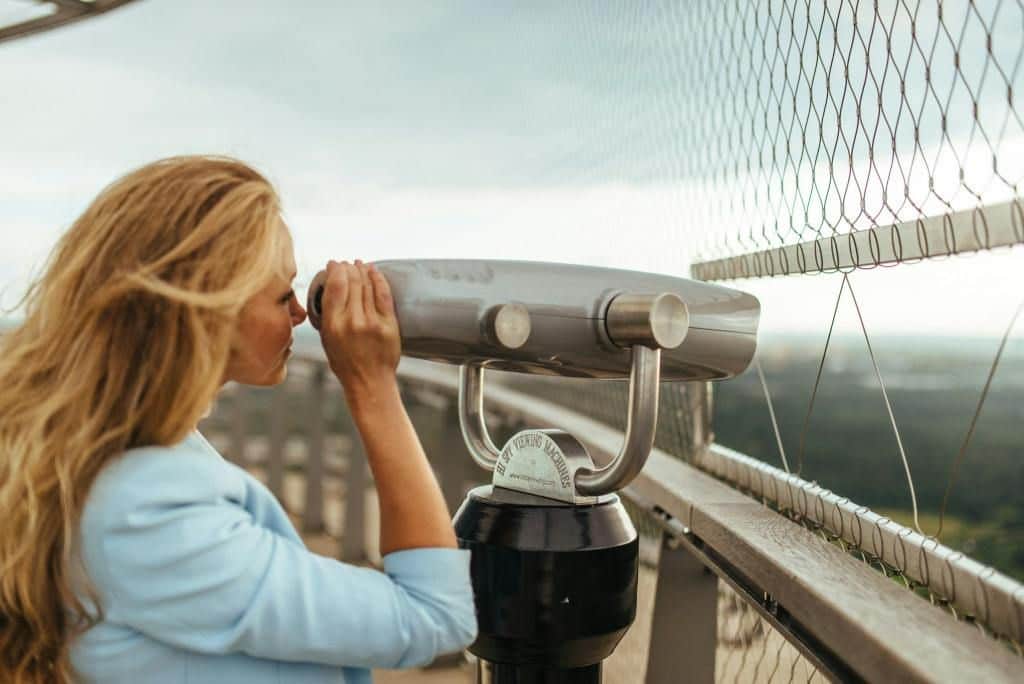 Tallinn TV Tower City Card (Tallinn) A person with long hair looks through a coin-operated binocular viewer on an outdoor observation deck.