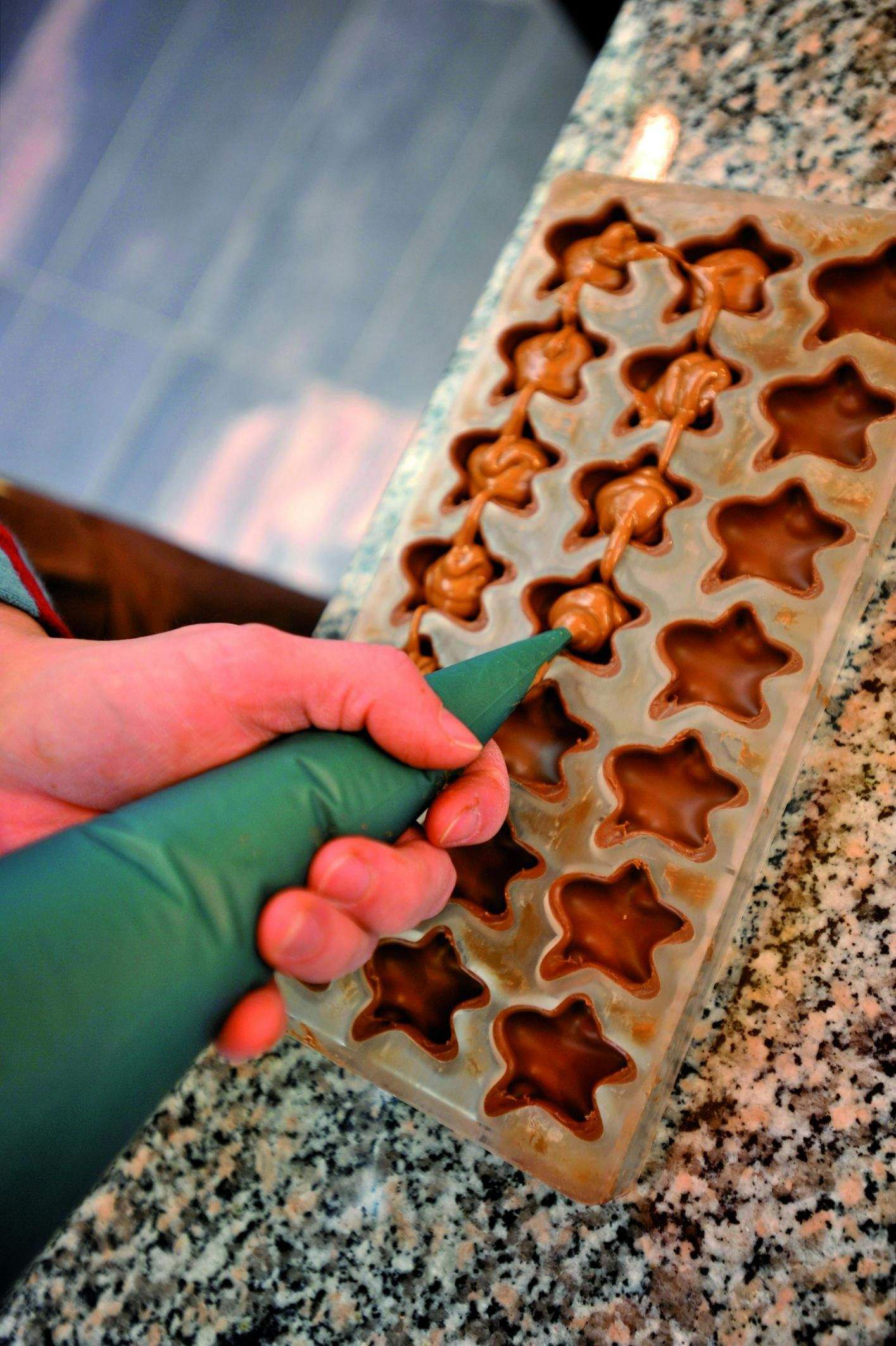 A hand filling star-shaped molds with chocolate using a green piping bag on a granite countertop.