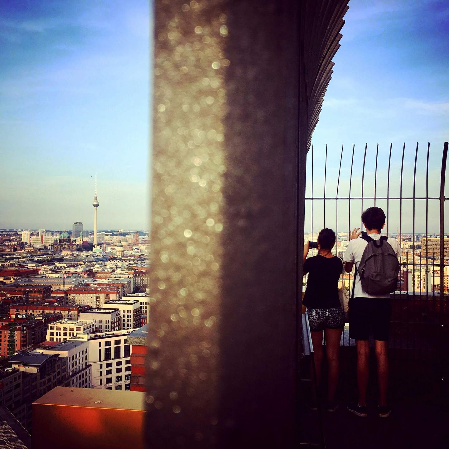 Panoramapunkt City Card (Berlin) Two people viewing a cityscape from a high observation deck, separated by a vertical partition. The skyline includes a prominent TV tower.