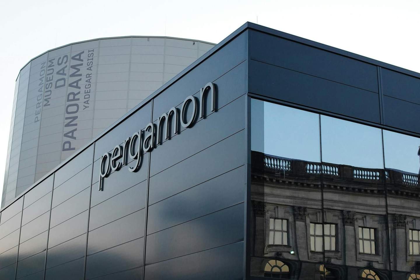 Modern building with "Pergamon" signage, reflective windows, and a cylindrical structure in the background labeled "Pergamon Museum DAS PANORAMA."