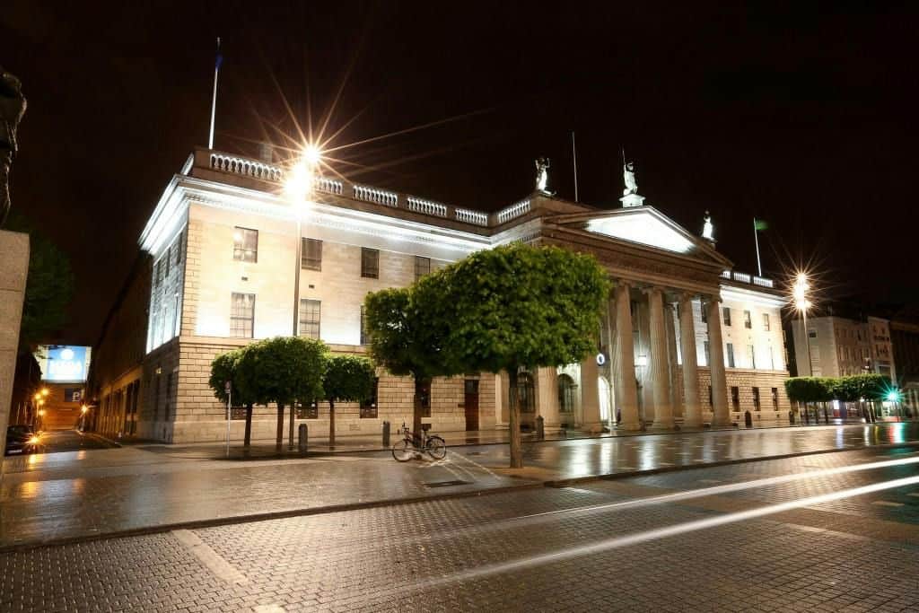 General Post Office Dublin City Cards & Passes (Dublin) Illuminated neoclassical building with columns and statues at night, surrounded by trees and a wet pavement reflecting lights.
