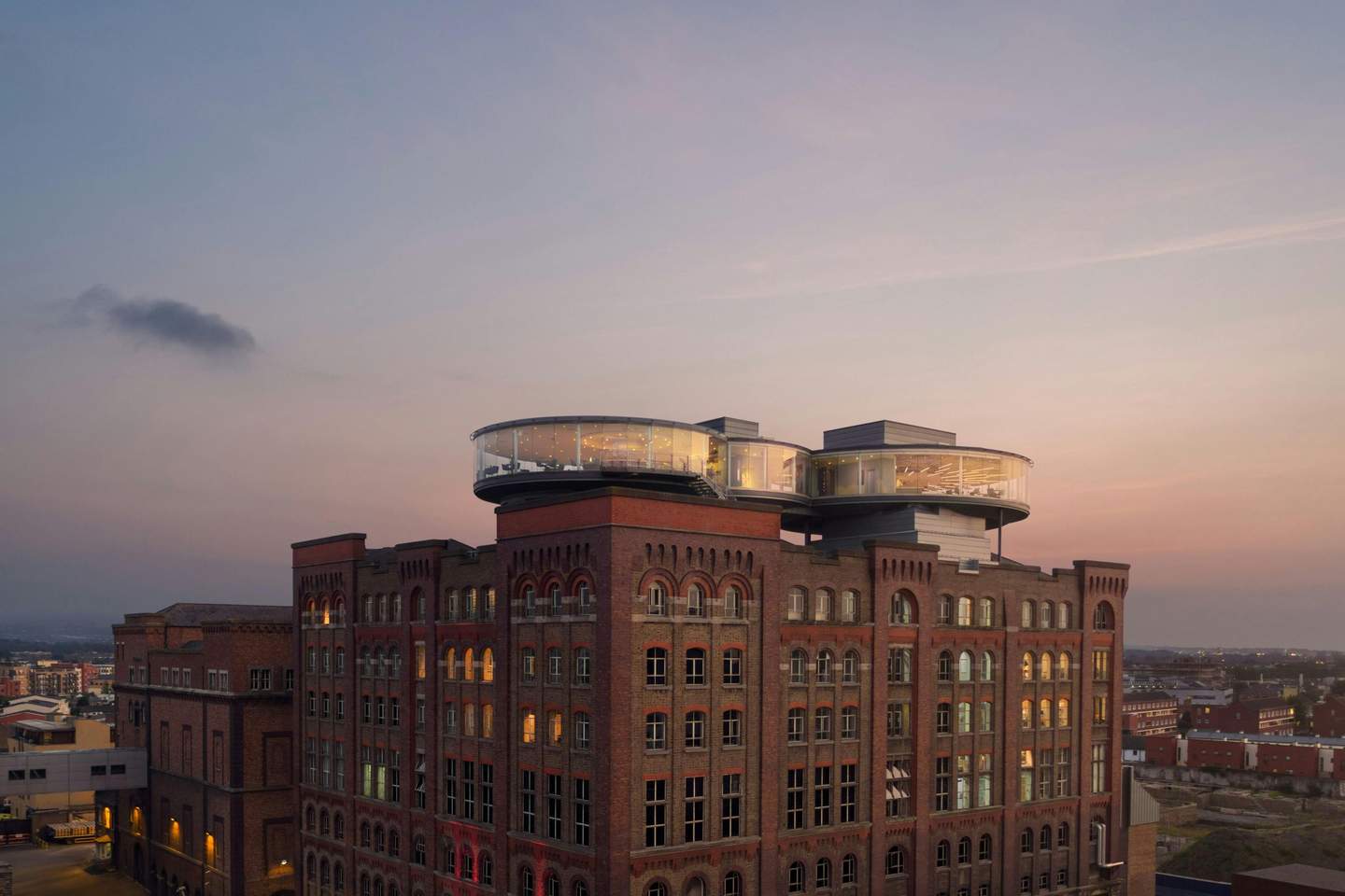 A red brick industrial-style building with modern glass circular extensions on the rooftop, set against a dusk sky.