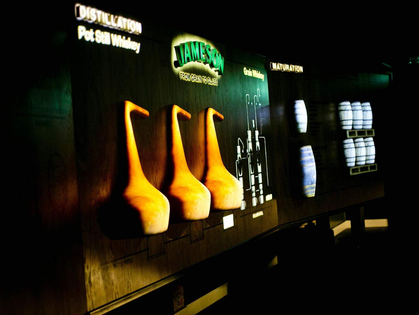 Backlit display showing different stages of whiskey production: distillation, grain whiskey, and maturation with accompanying images.