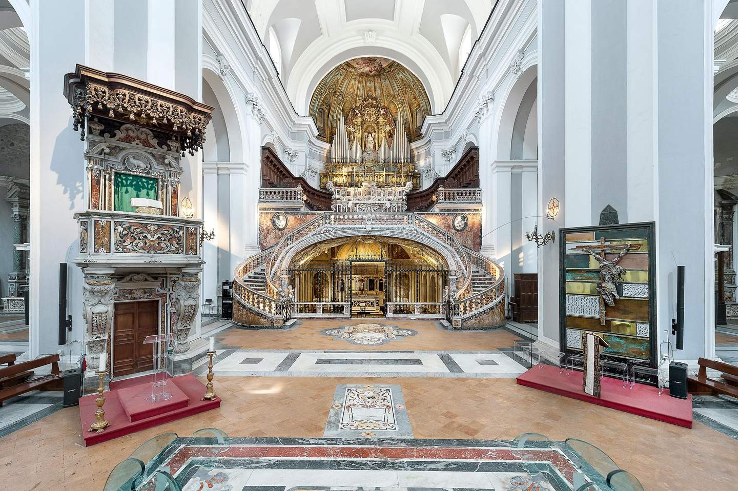 An ornate church interior with a grand altar, a gilded organ, curved staircases, and intricate architectural details.