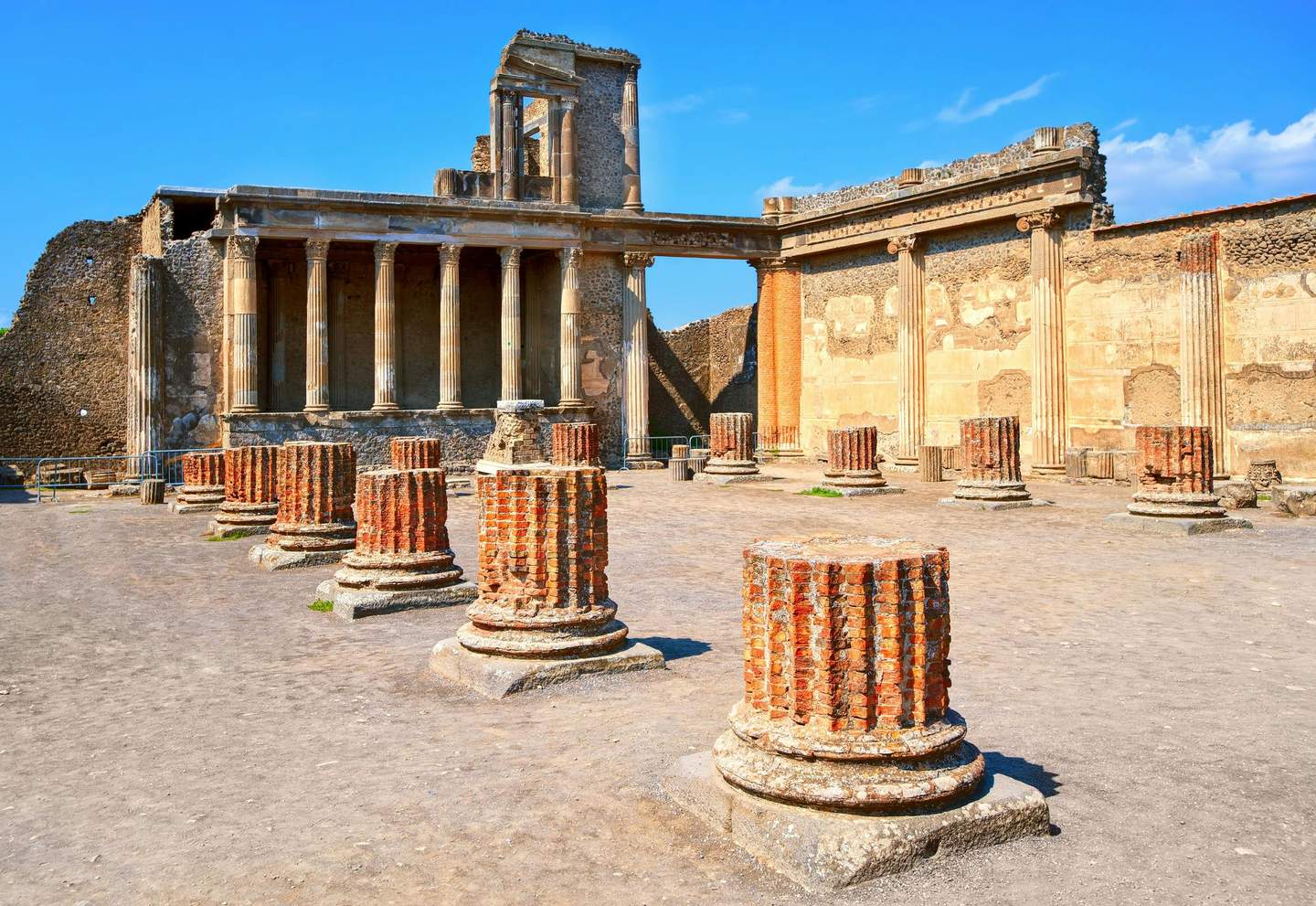 Pompeï Citycards & Passen (Pompeii) Oude ruïnes met staande zuilen en bakstenen stronken, met verweerde stenen muren, tegen een helderblauwe lucht.