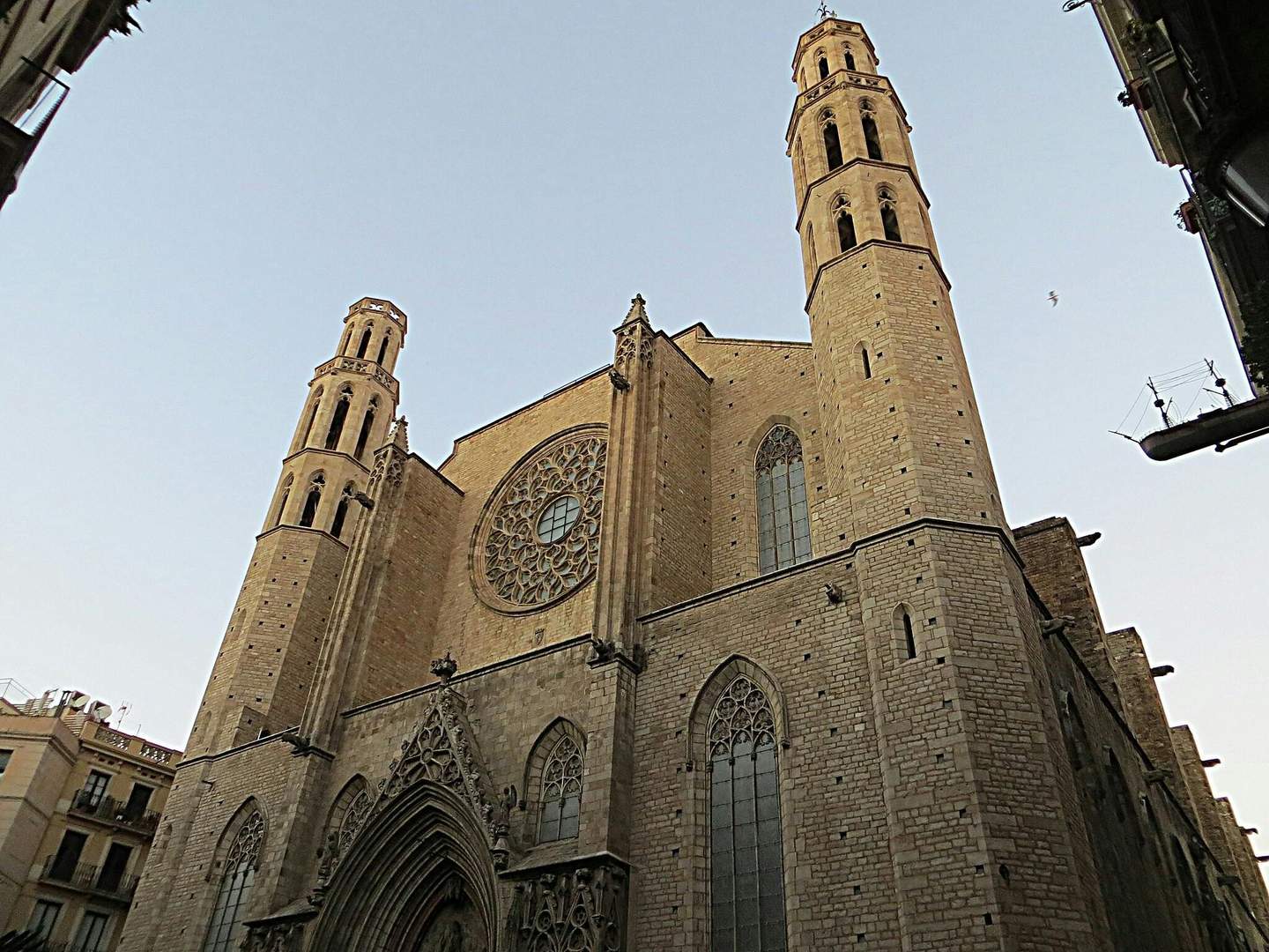 Une grande église gothique en pierre, dotée de deux clochers, d'une grande rosace et d'une entrée en arc brisé, se détachant sur un ciel clair.
