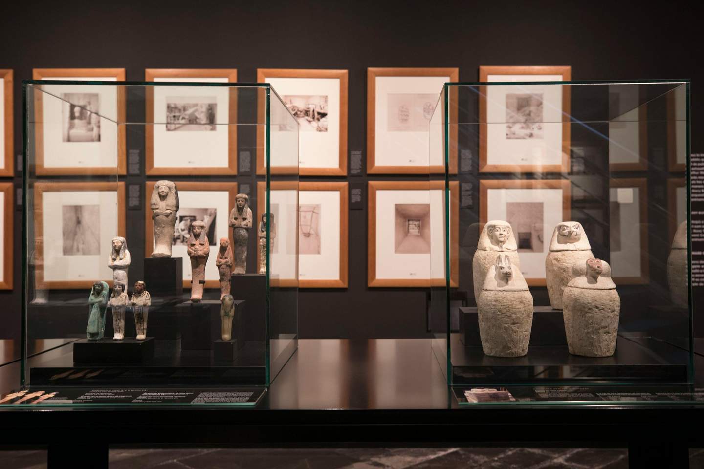 Des objets anciens exposés dans des vitrines, avec des photographies encadrées sur le mur derrière eux, dans le cadre d'un musée.