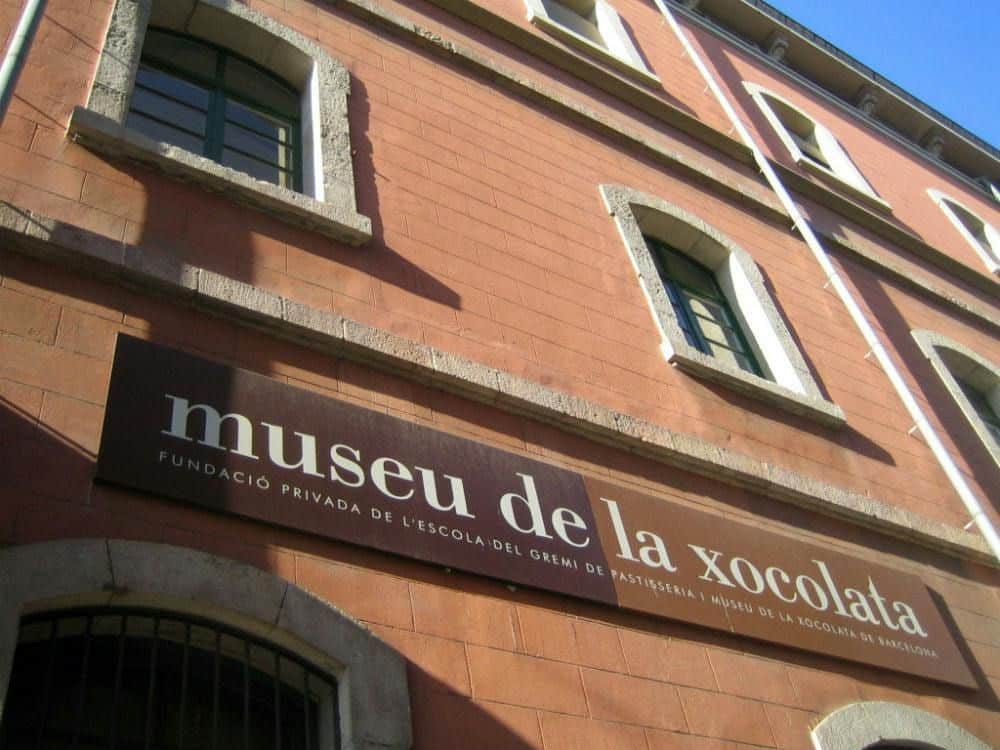 바르셀로나 소콜라타 박물관 시티 카드 및 패스 (바르셀로나) "museu de la xocolata" 라고 적힌 커다란 간판과 여러 개의 아치형 창문이 있는 건물 외부.