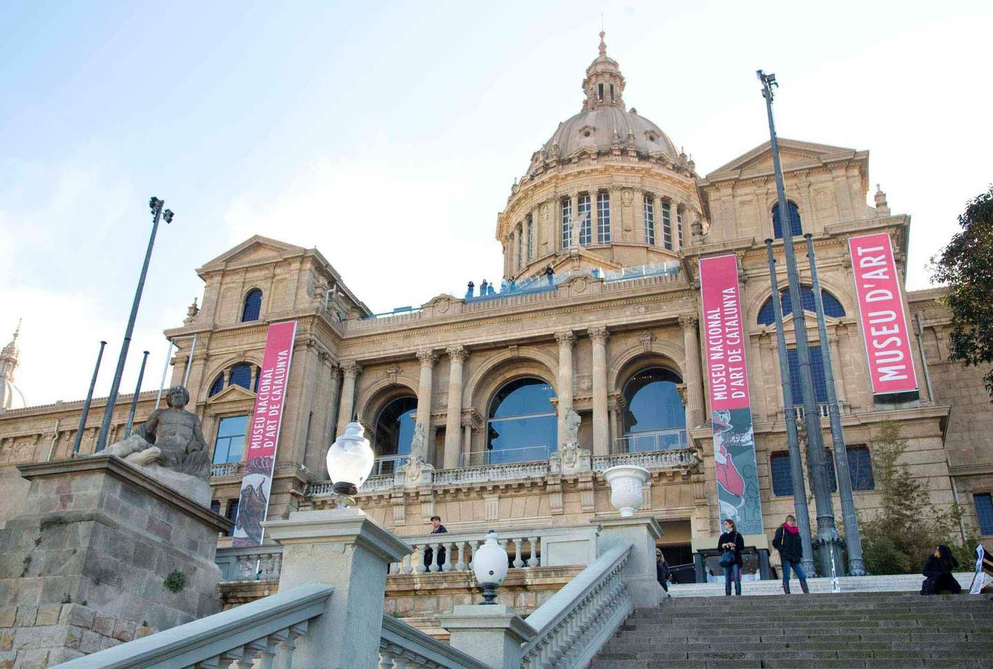Vista frontal del Museu Nacional d'Art de Catalunya, amb grans pancartes, columnes de pedra i una escala amb gent.
