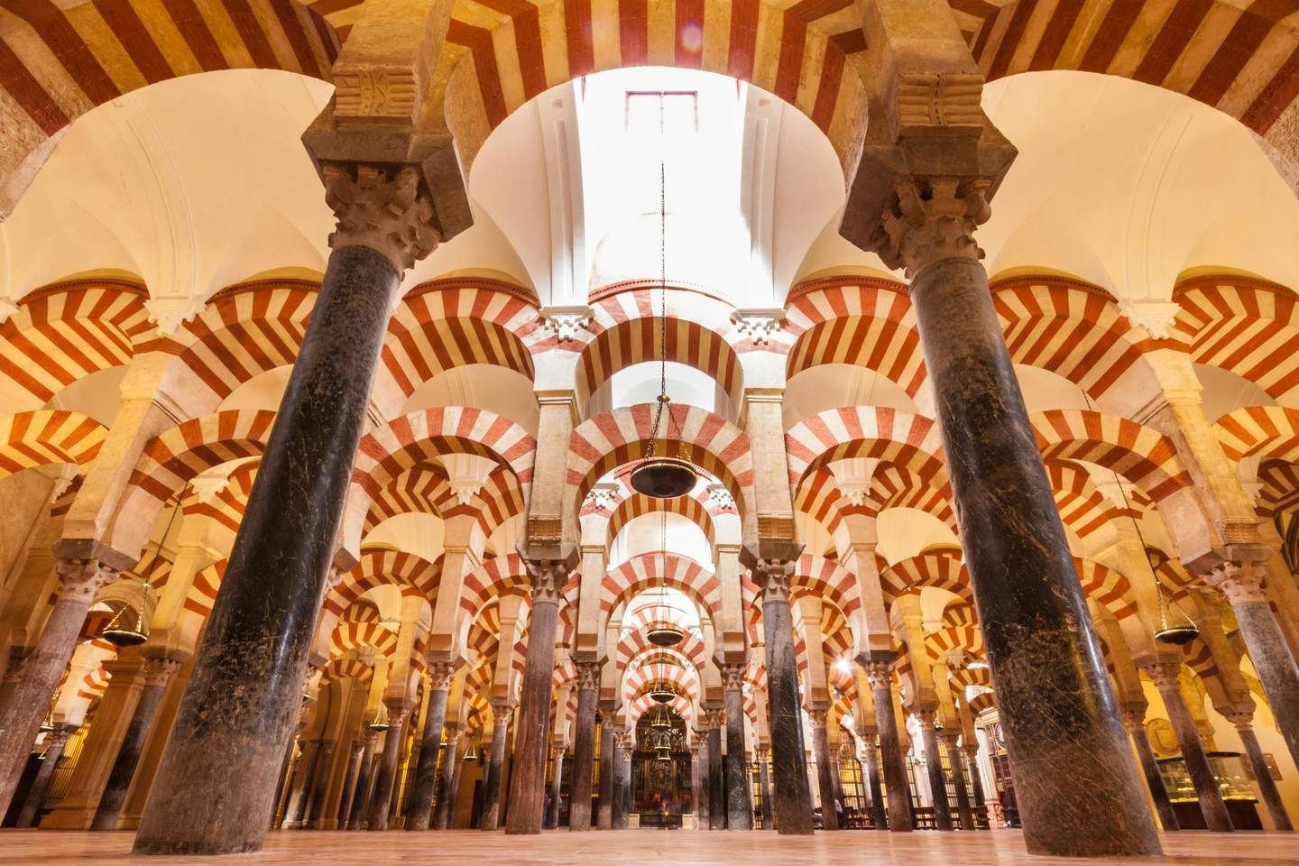 A series of ornate red and white arches supported by stone columns in a historic, cavernous interior space.