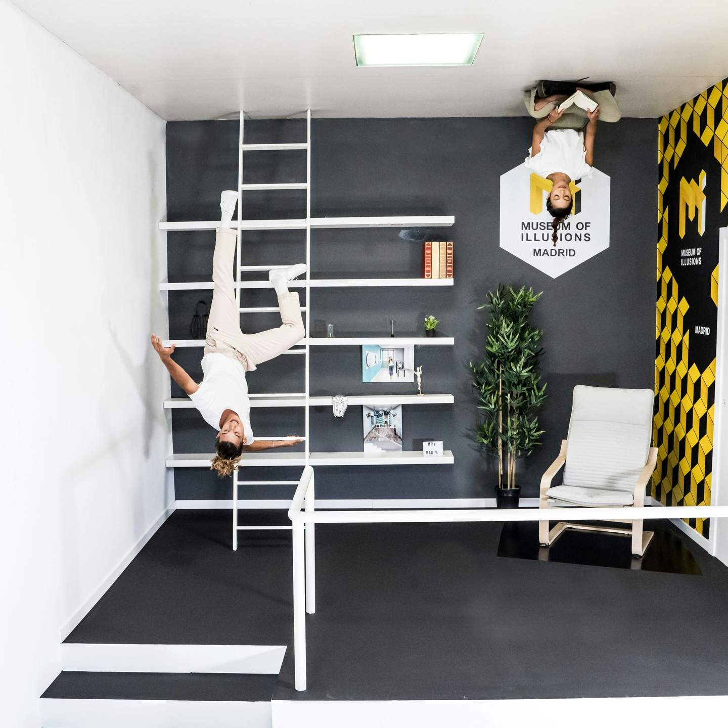 Museum of Illusions Madrid City Card (Madrid) Two people appear upside down in an optical illusion room at the Museum of Illusions Madrid, with furniture and shelves on the walls.