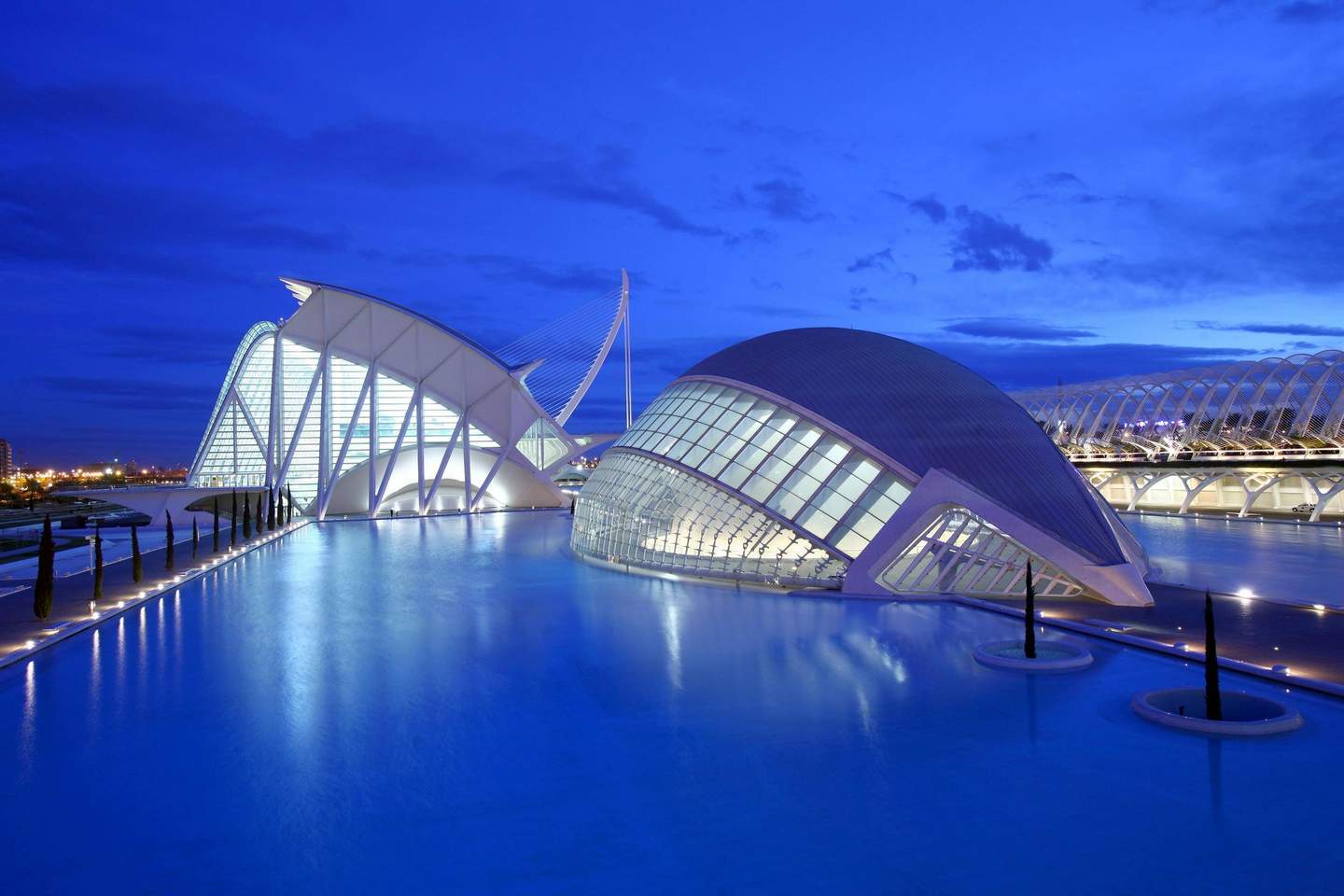 Hemisfèric City Card (València) Modern futuristic buildings with white structures and large glass windows, surrounded by a reflecting pool under a twilight sky.