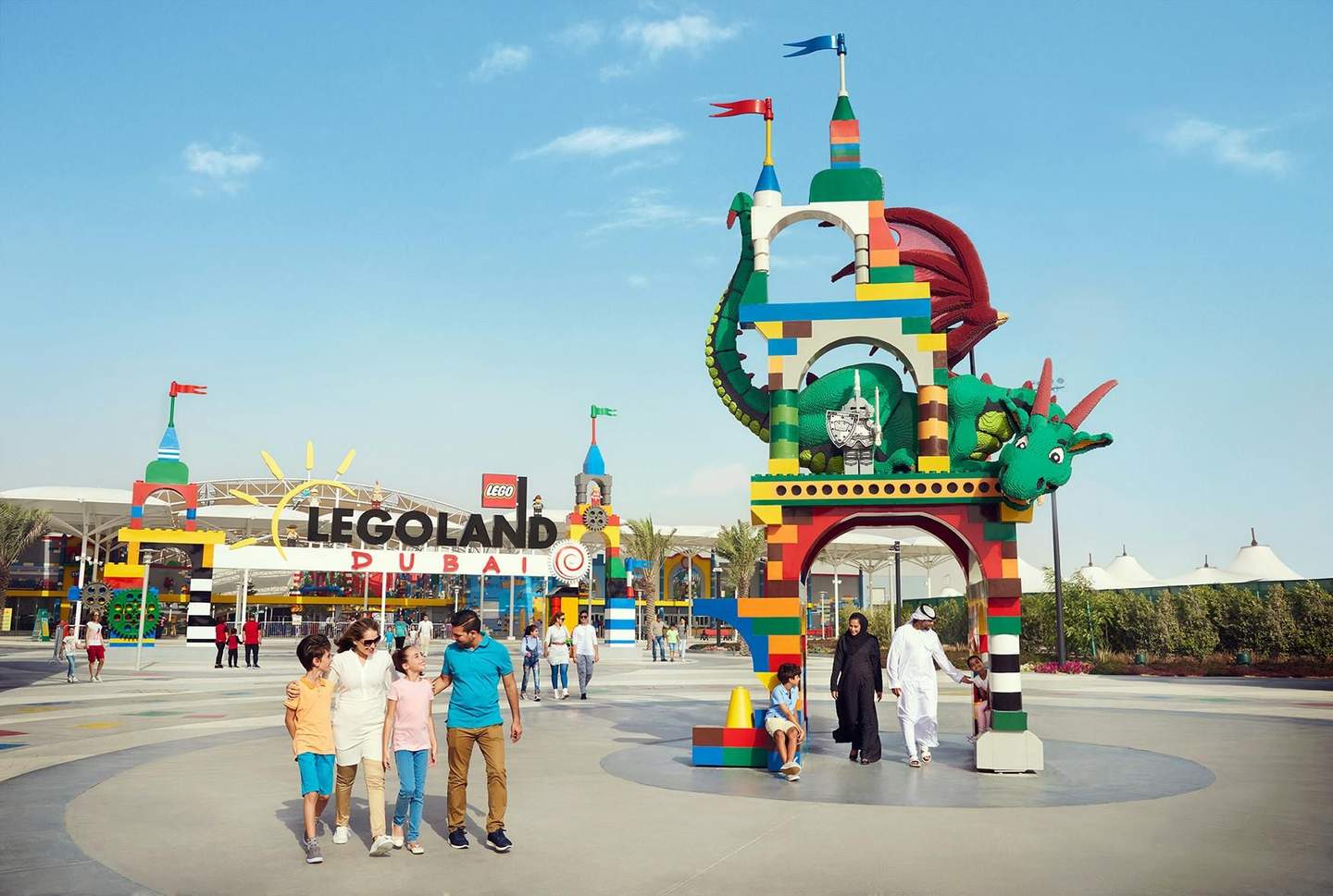 Families walk near the colorful entrance of LEGOLAND Dubai, featuring a large LEGO dragon and vibrant archway under a clear sky.