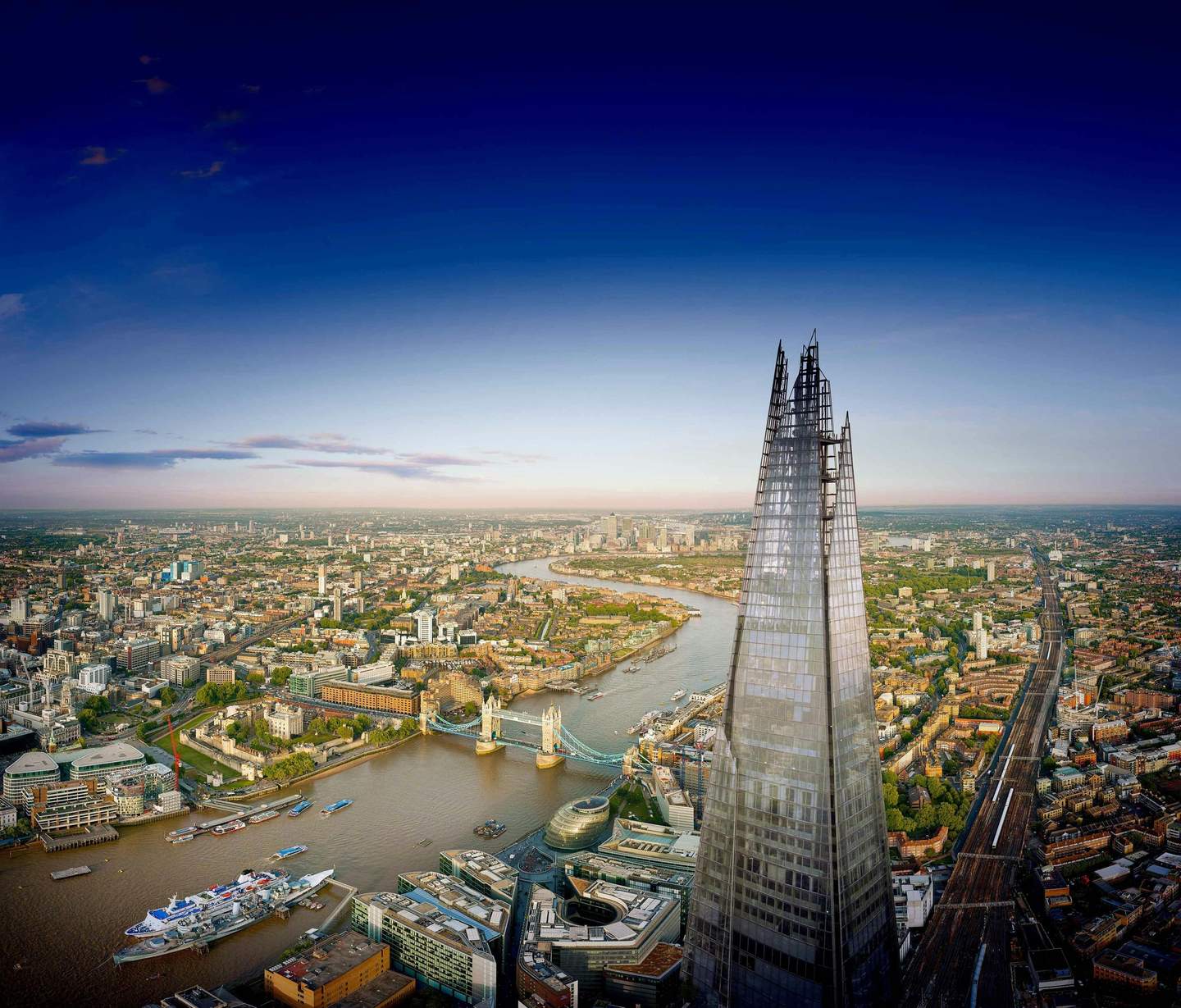 The View from The Shard Aerial view of The Shard skyscraper in London with the River Thames, Tower Bridge, and cityscape under a vivid blue sky.