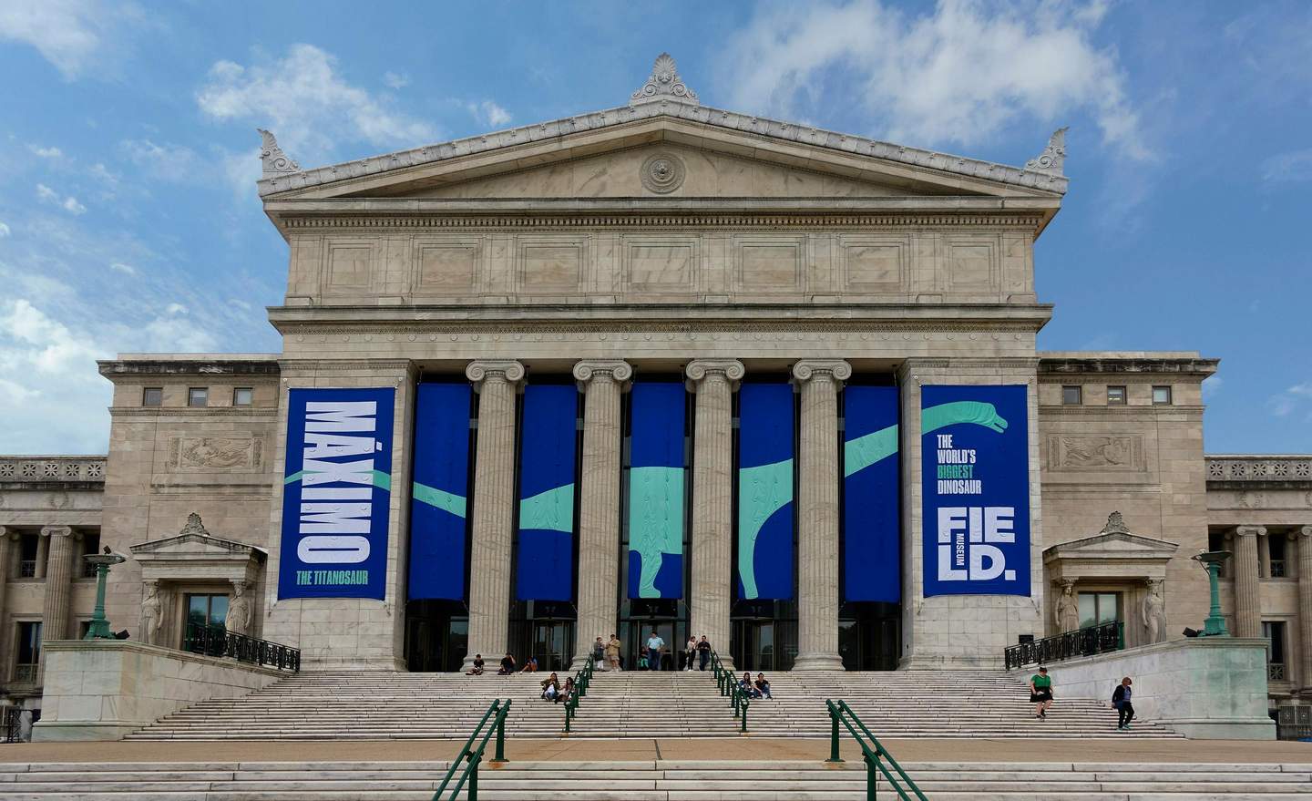 Museum of Science & Industry Chicago City Cards & Passes (Chicago) Large, classical-style building with columns and banners promoting "Máximo The Titanosaur" exhibit. People sit on the steps.