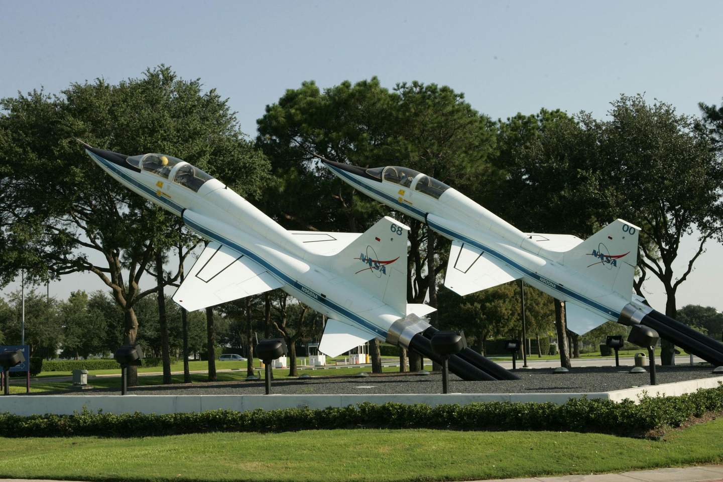 Space Center Houston City Card (Houston) Two jet aircraft on display at an outdoor exhibit, positioned nose-up, surrounded by trees and greenery.