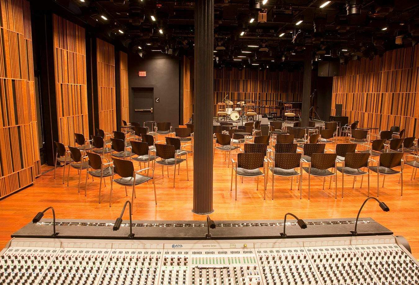 New Orleans Jazz Museum Lege muziekzaal met mengpaneel, rijen stoelen en een podium met een drumstel en muziekapparatuur.