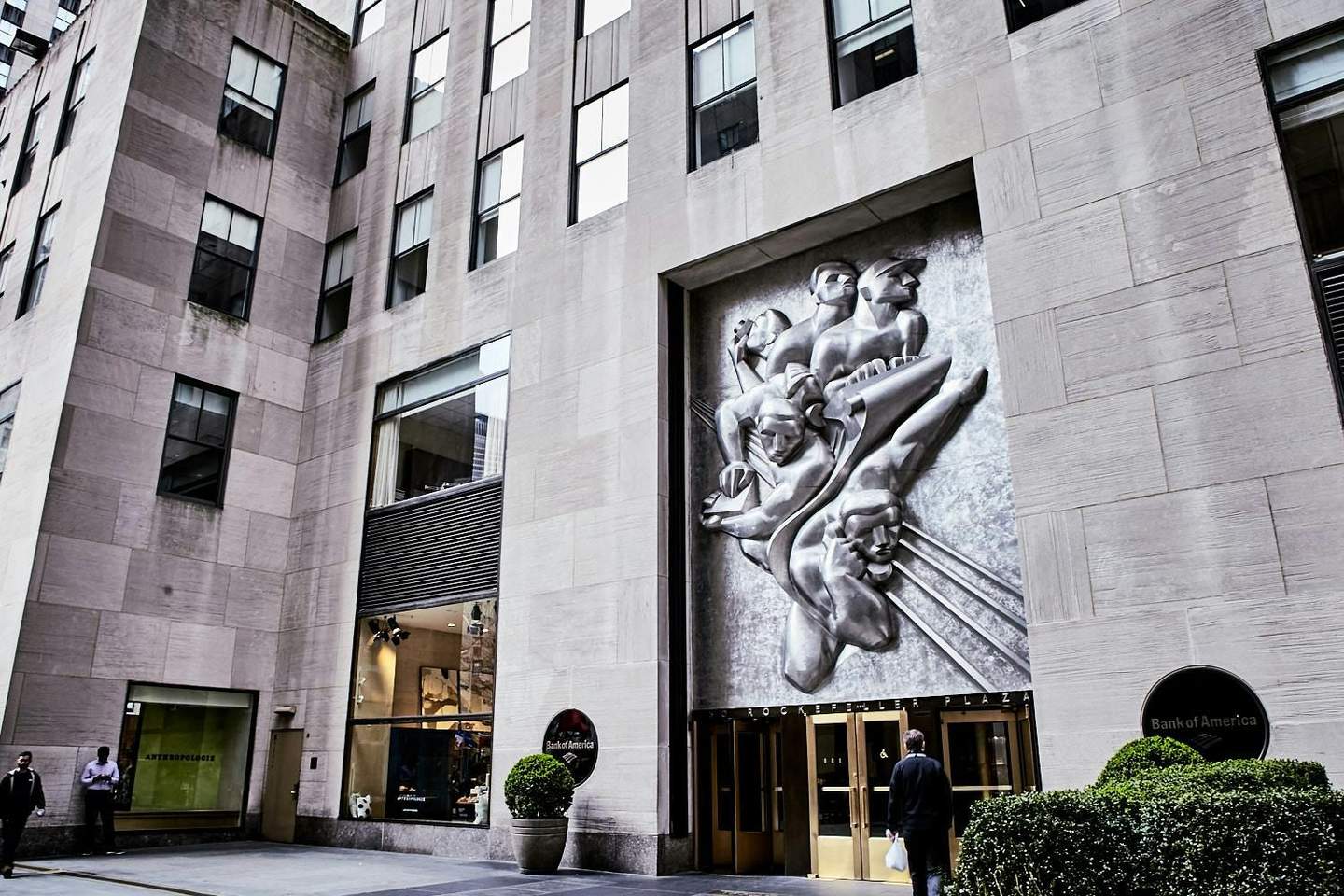 Rockefeller Center City Cards & Passes (New York) Large stone building with high windows, a metal relief sculpture, entrance doors labeled "Rockefeller Plaza," and Bank of America signage.