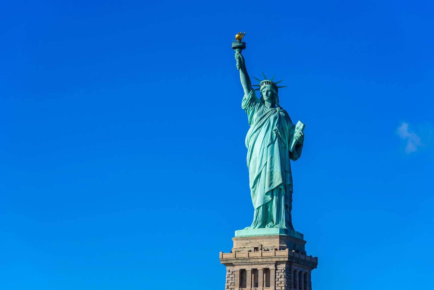 The Statue of Liberty, holding a torch and a tablet, stands against a clear blue sky.