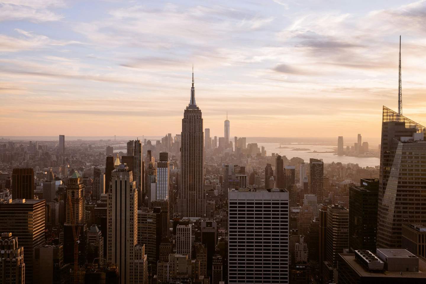 Top of the Rock City Cards & Passes (New York) View of a city skyline at sunset, dominated by tall skyscrapers, with a river and distant buildings in the background.