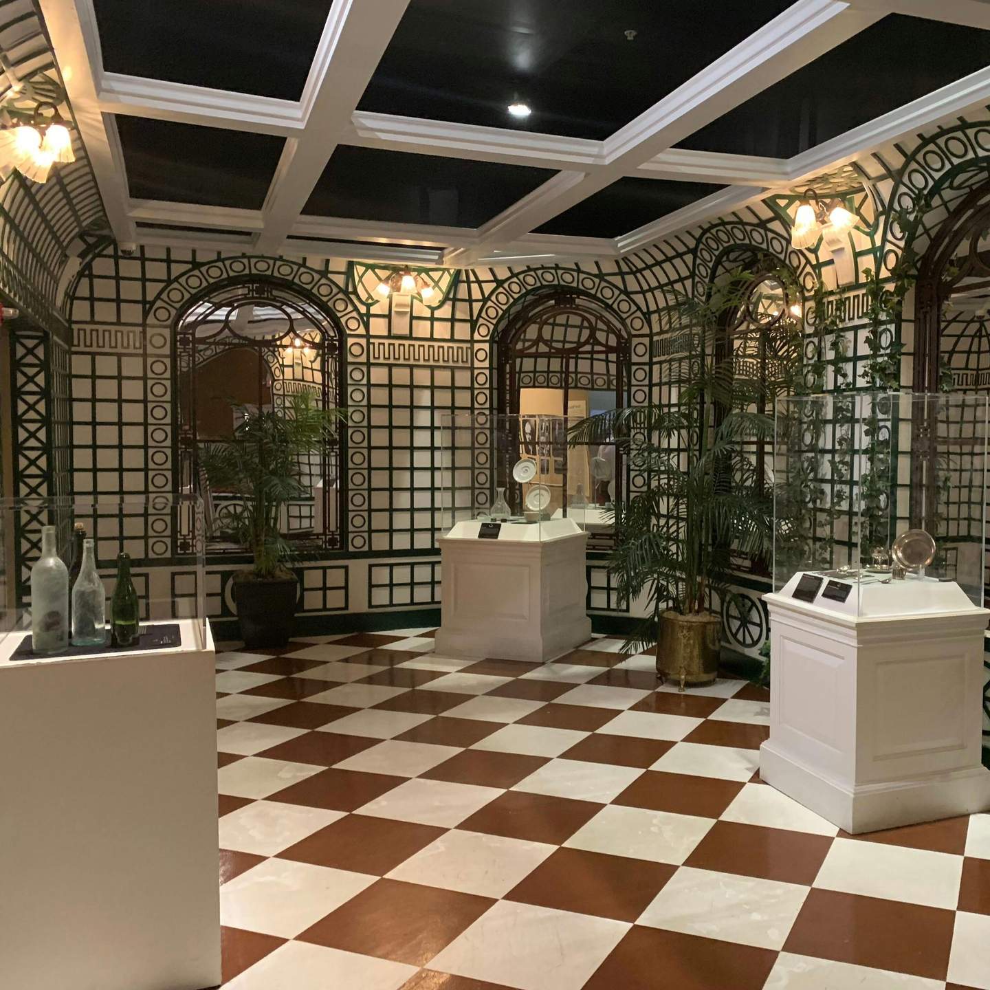Titanic: The Artifact Exhibition Orlando Stanza con pavimento a scacchi, pareti decorative, piante in vaso e vetrine con manufatti.