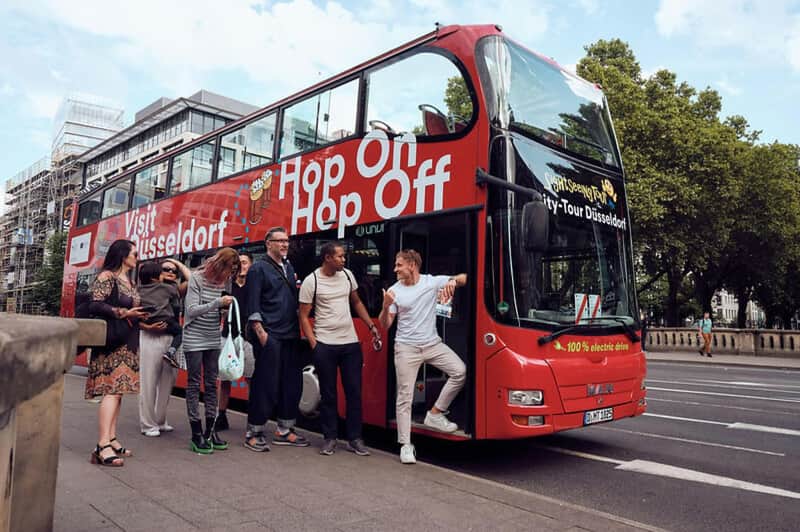 A group of people standing near a red double-decker sightseeing bus with "Hop On Hop Off" written on its side.