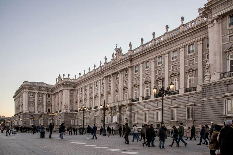 Large stone building with ornate details and columns, surrounded by numerous pedestrians on a spacious paved plaza.