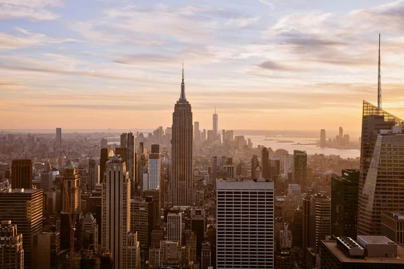 RockMoMA – Top of the Rock & The Museum of Modern Art (MoMA) A cityscape featuring the Empire State Building at sunset, with surrounding skyscrapers and a golden sky.