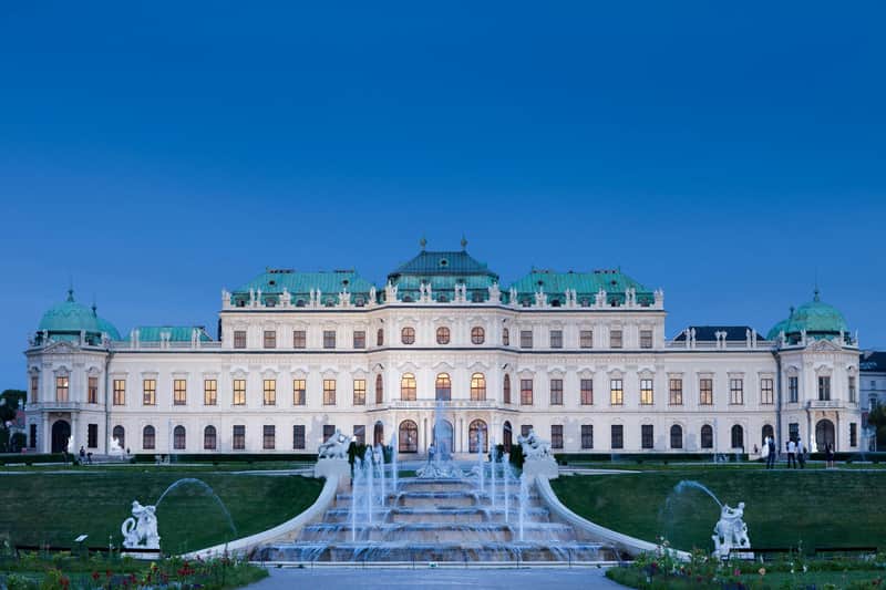 Belvedere Palace City Card (Vienna) An ornate palace with green domes, fountains, statues, and gardens, set against a clear blue sky at dusk.