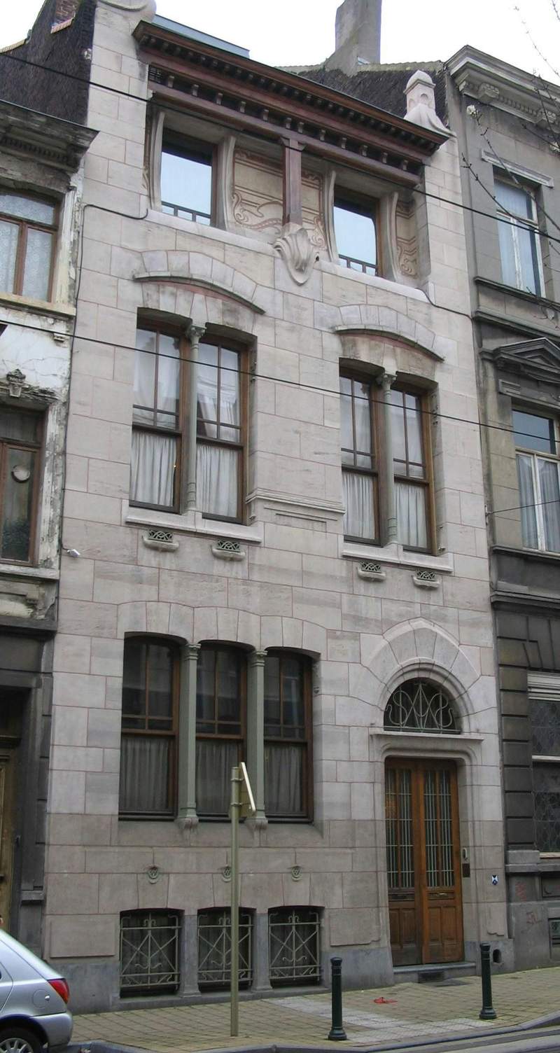 Three-story stone building with arched windows and intricate architectural details. Wooden door at the street level.
