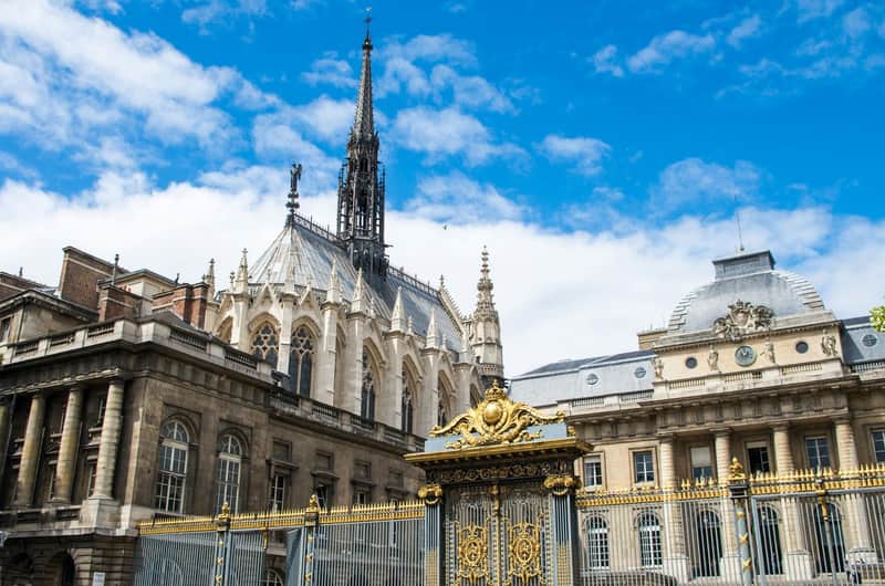 Historic Gothic cathedral and palace with ornate gold gate under a blue sky with scattered clouds.