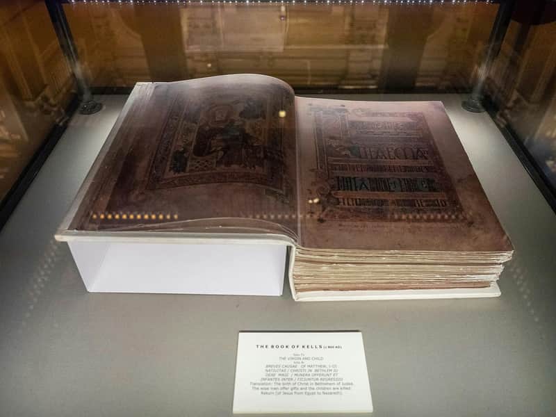 An illuminated manuscript, "The Book of Kells," displayed in a glass case with a description plaque below.