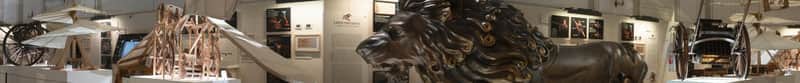 Museum display with wooden models of mechanical inventions, a large lion sculpture, and informative panels on the walls.