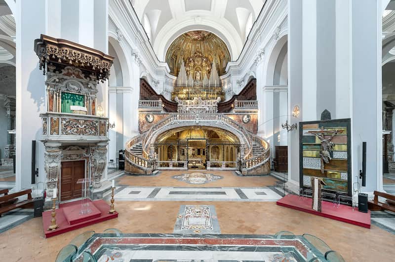 An ornate church interior with a grand altar, a gilded organ, curved staircases, and intricate architectural details.