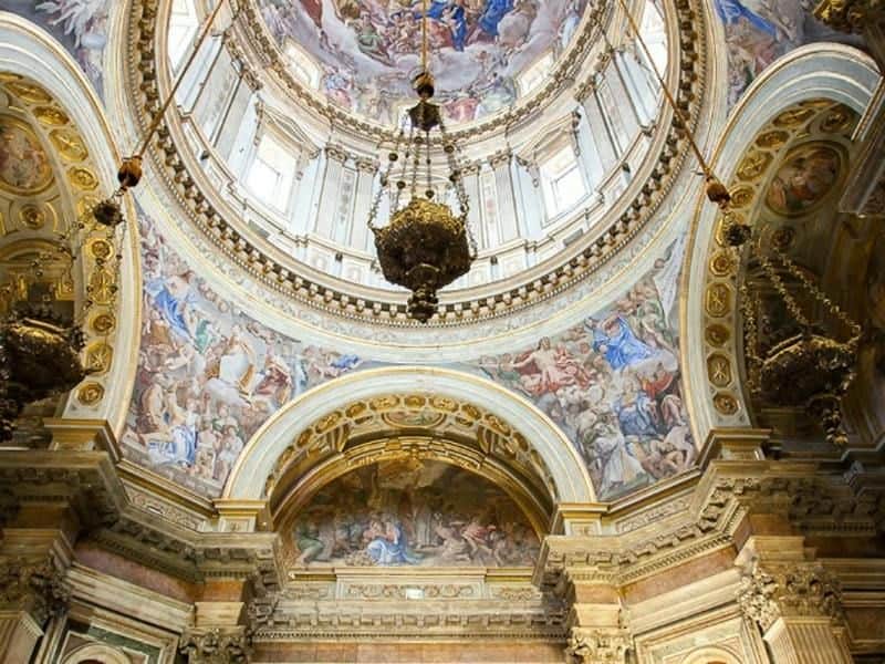 Ornate church interior with a large dome ceiling, elaborate frescoes, and a central chandelier. Golden arches and intricate details.