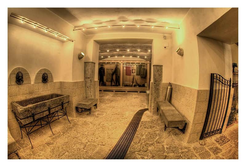 A well-lit, stone-walled hallway with benches, lion-shaped water fountains, and mannequins in uniforms displayed behind glass.