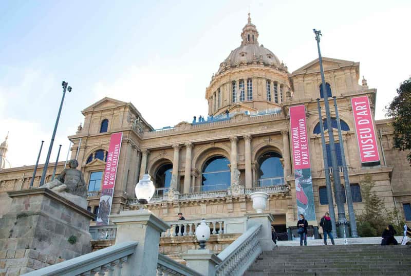 Museu Nacional d'Art de Catalunya Bykort & Pas (Barcelona) Forsidebillede af Museu Nacional d'Art de Catalunya med store bannere, stensøjler og en trappe med mennesker.