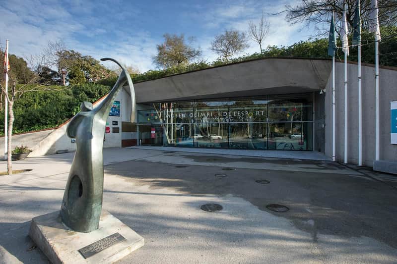 Olympisk og Sportsmuseum Joan Antoni Samaranch Bykort & Pas (Barcelona) Indgangen til Museu Olímpic i de l'Esport, med en moderne skulptur til venstre og en glasfacade med tekst. Træer i baggrunden.
