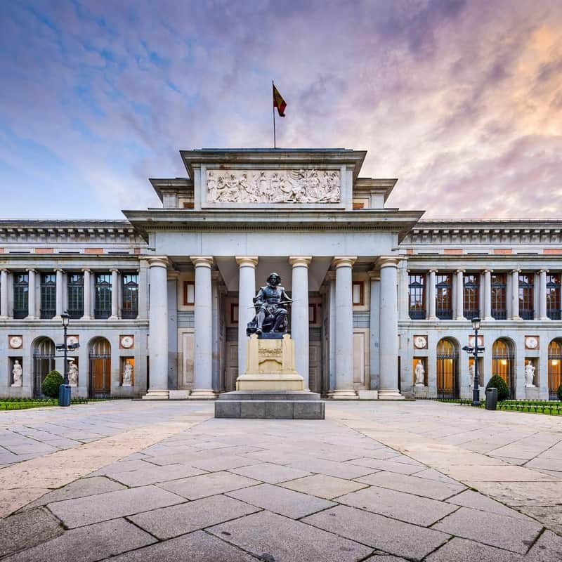 Grand neoclassical building with a statue in front, columns, sculptures, a relief, and a flag atop, under a colorful sky.