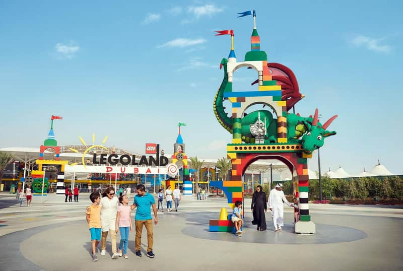 Entrance of LEGOLAND Dubai with colorful LEGO structures, people walking, and a large dragon decoration under a clear blue sky.