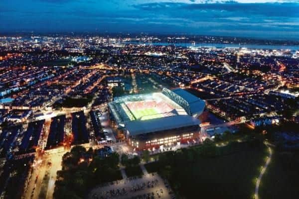 Luftfoto af et stærkt oplyst stadion midt i byens lys i skumringen, med omkringliggende bolig- og byområder.