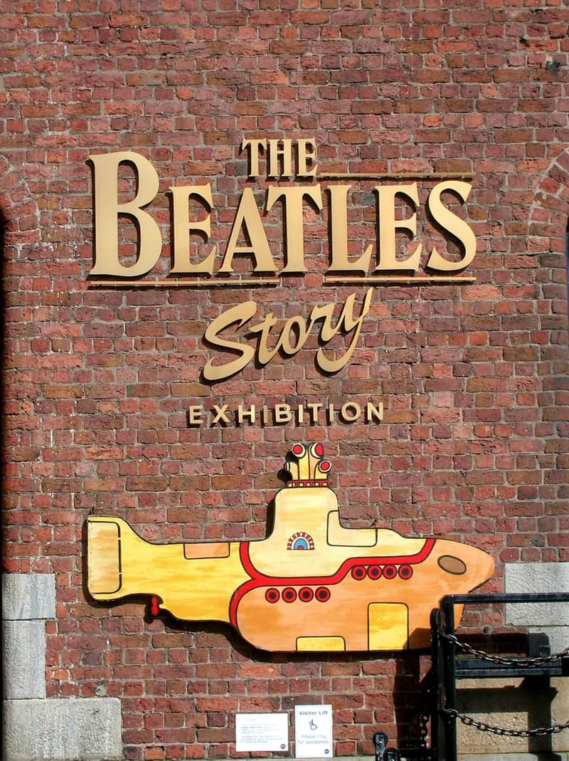 Signa en una paret de maons amb "The Beatles Story Exhibition" i una il·lustració submarina pintada de groc.