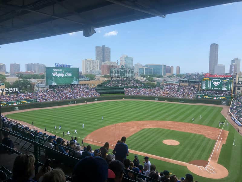 Wrigley Field during a baseball game, crowded stands, players on the field, and the scoreboard displaying "Welcome to Wrigley Field."